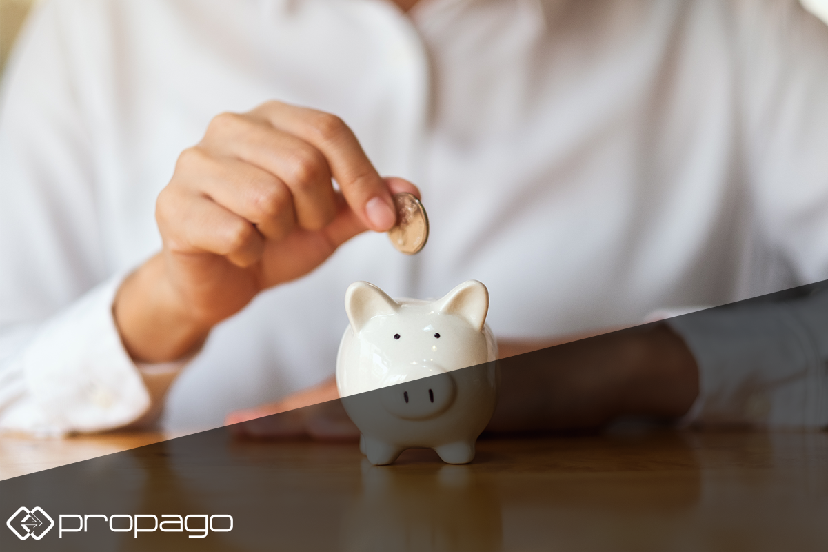 Hand placing a coin into a white piggy bank, symbolizing budget savings and financial management in marketing.
