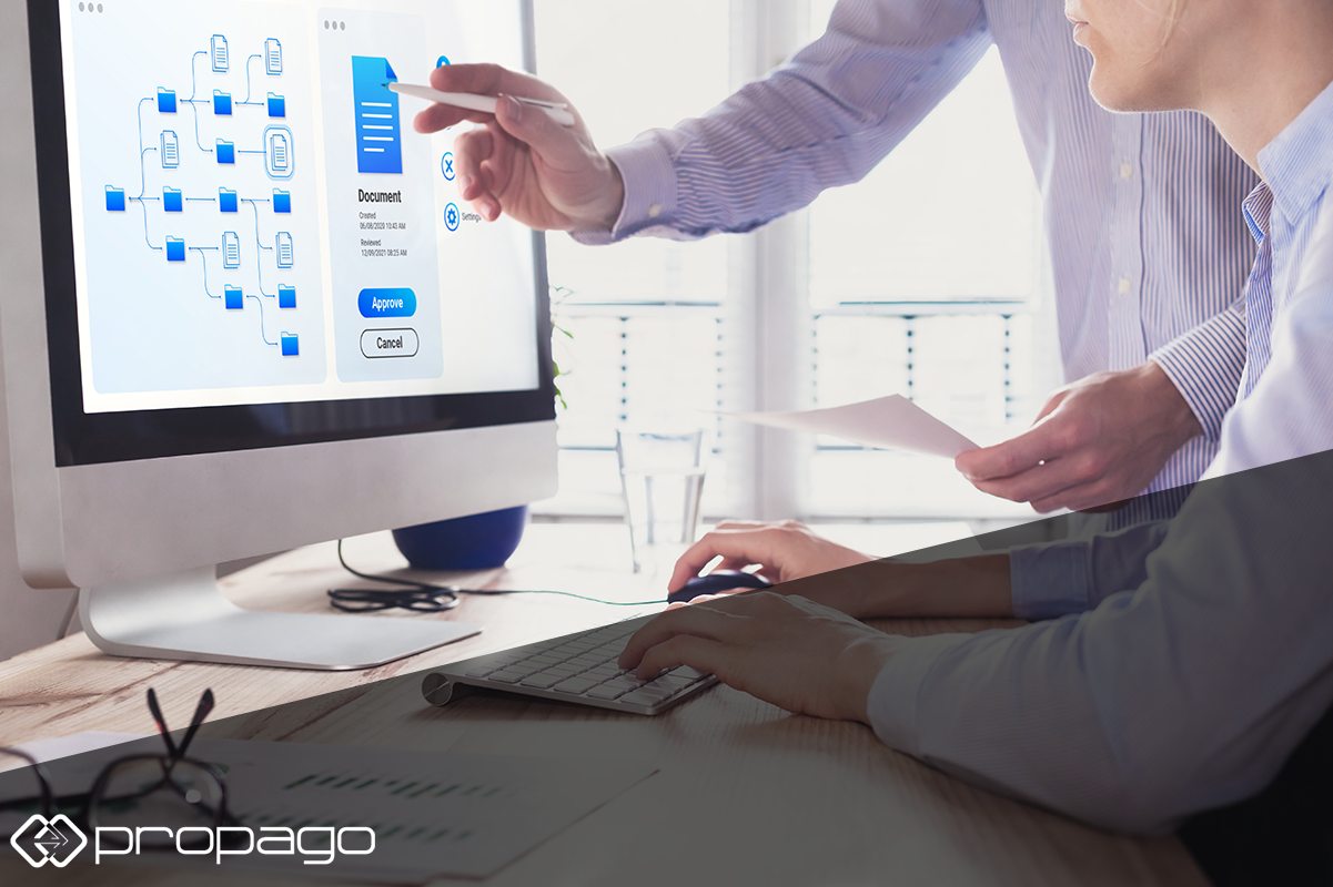 Person pointing at digital asset management interface on a computer screen, illustrating document approval process, with another person using a keyboard, emphasizing the integration of digital asset management in marketing solutions for print providers.