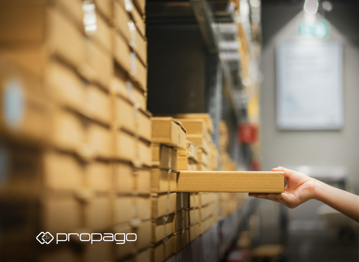 Hand reaching for a brown box on a shelf in a warehouse, illustrating kitting and logistics in the printing industry, relevant to web-to-print solutions by Propago.